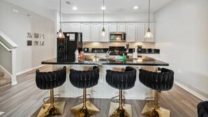 A modern kitchen with white cabinets, a black island, and three black bar stools with gold bases. - Luxury 4BR Pool Home Near Disney (Davenport)