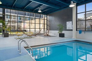 An indoor swimming pool with clear glass walls, a tiled floor, and a hammock chair.
