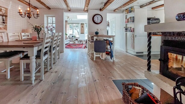 Ein geräumiger Wohnbereich mit Holzboden, einem Esstisch mit Stühlen, einem Kamin und einer Küchenzeile mit Schränken und einem Herd.