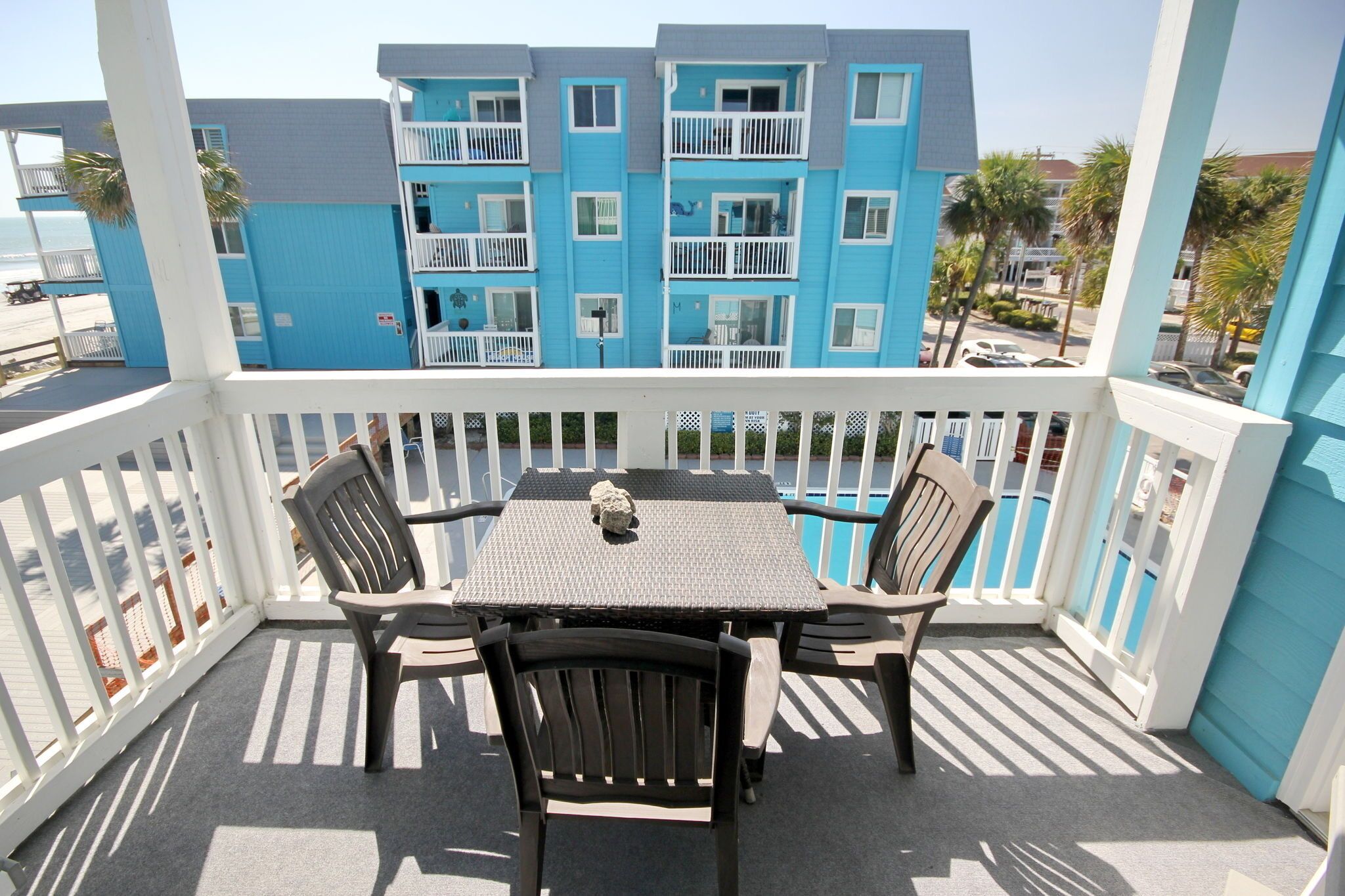 A balcony with a table and chairs, overlooking a blue building with balconies.