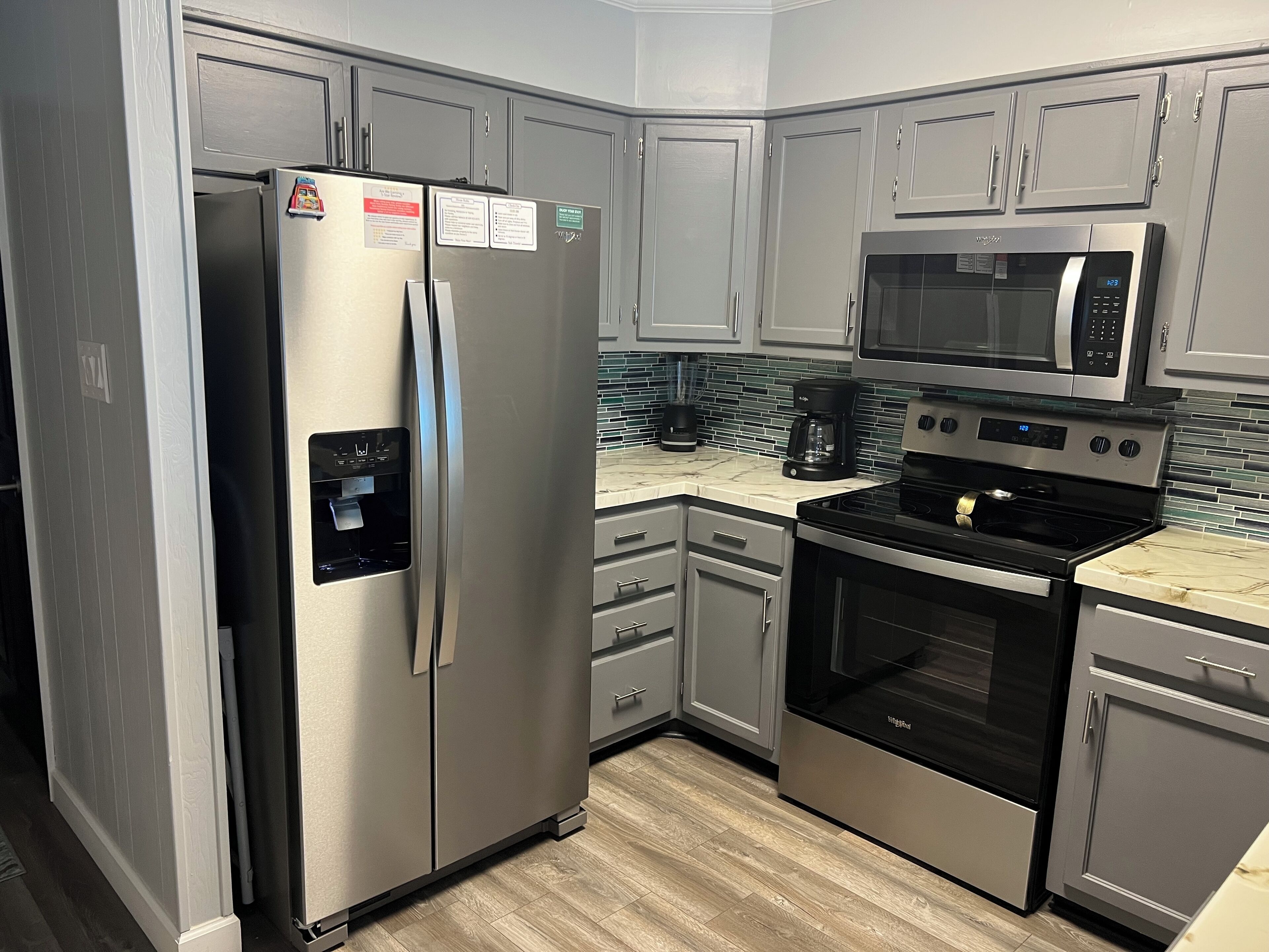 A modern kitchen with stainless steel appliances, grey cabinets, and a tiled backsplash.