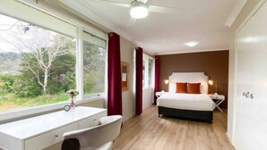 Ein Schlafzimmer mit Bett, Schreibtisch und Stuhl, mit einem Fenster und Blick auf Bäume.