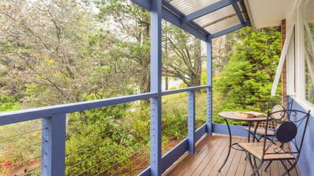 Ein überdachter Balkon mit Tisch und Stühlen, umgeben von viel Grün.