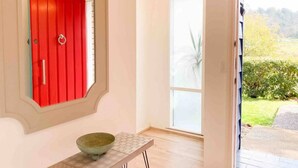 Ein Zimmer mit roter Tür, einem Fenster mit Blick auf Grünflächen und einem kleinen Tisch mit einer Schüssel.