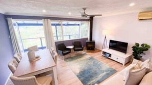 Ein modernes Wohnzimmer mit Essbereich, Kamin, Fernseher und einem großen Fenster mit Vorhängen.
