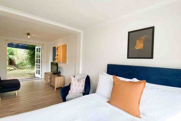 A bedroom with a bed, a chair, a TV, and a door leading to a garden.