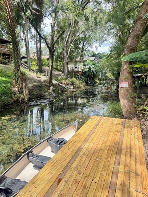 A wooden dock extending into a calm river surrounded by lush greenery and trees.