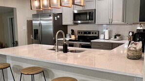 A modern kitchen with a large island, stainless steel appliances, and wooden bar stools.