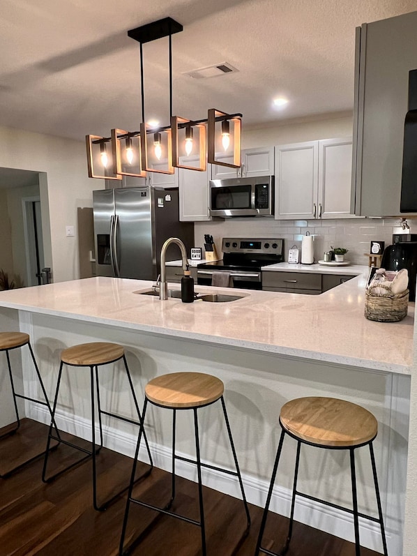A modern kitchen with a large island, stainless steel appliances, and wooden bar stools.