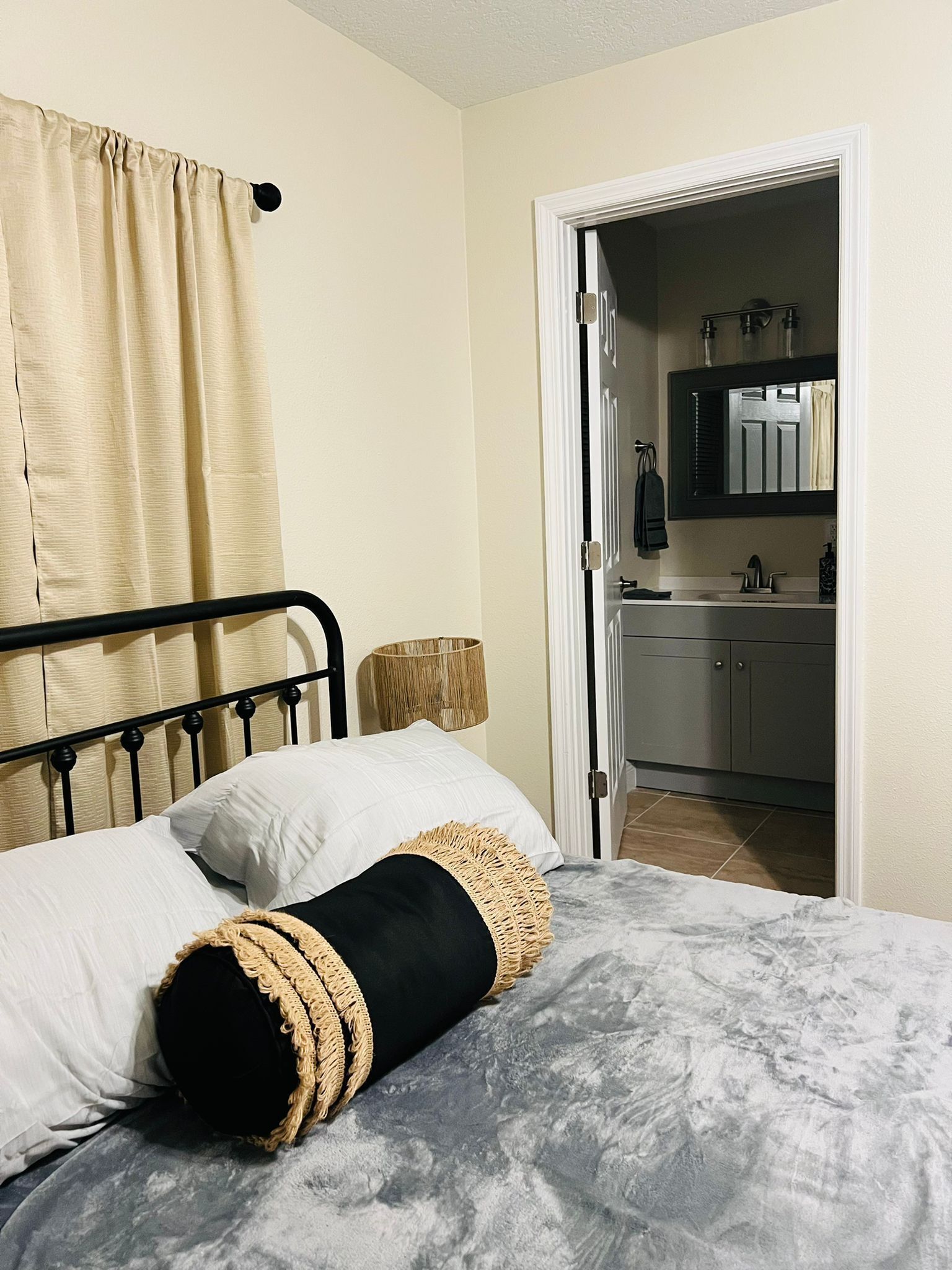Une chambre à coucher avec un lit, une lampe de chevet et une salle de bain visible à travers une porte ouverte.