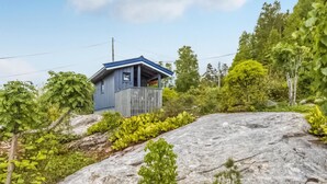 En liten, envåningsbyggnad med ett blått tak, omgiven av frodig grönska och en stor sten i förgrunden.