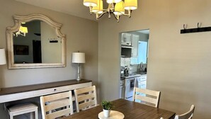 Un coin repas avec une table en bois, des chaises blanches, un lustre et un miroir au mur.