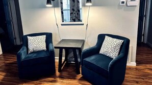 Une pièce comprenant deux fauteuils bleu foncé à motifs pois, une petite table en bois et un miroir décoratif agrémenté de deux lampes fixées au mur.