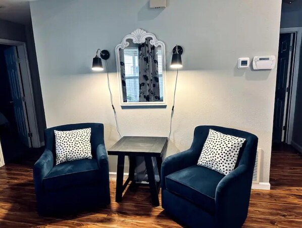A room with two dark blue armchairs with polka dot cushions, a small wooden table, and a decorative mirror with two wall-mounted lamps.