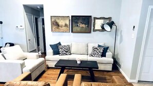 Un salon avec un canapé blanc, deux fauteuils en cuir marron, une table basse noire et deux tableaux encadrés accrochés au mur.