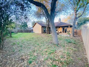 A residential backyard with a house, a large tree, and a wooden fence. - Spacious 3 BDRM for 9 - SA & NB (Live Oak)