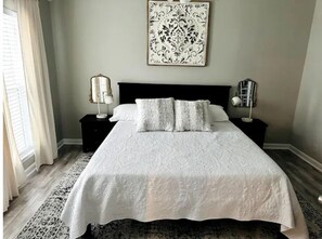 A neatly made bed with a white bedspread and two pillows, a black headboard, a wall-mounted artwork, and two bedside tables with lamps.