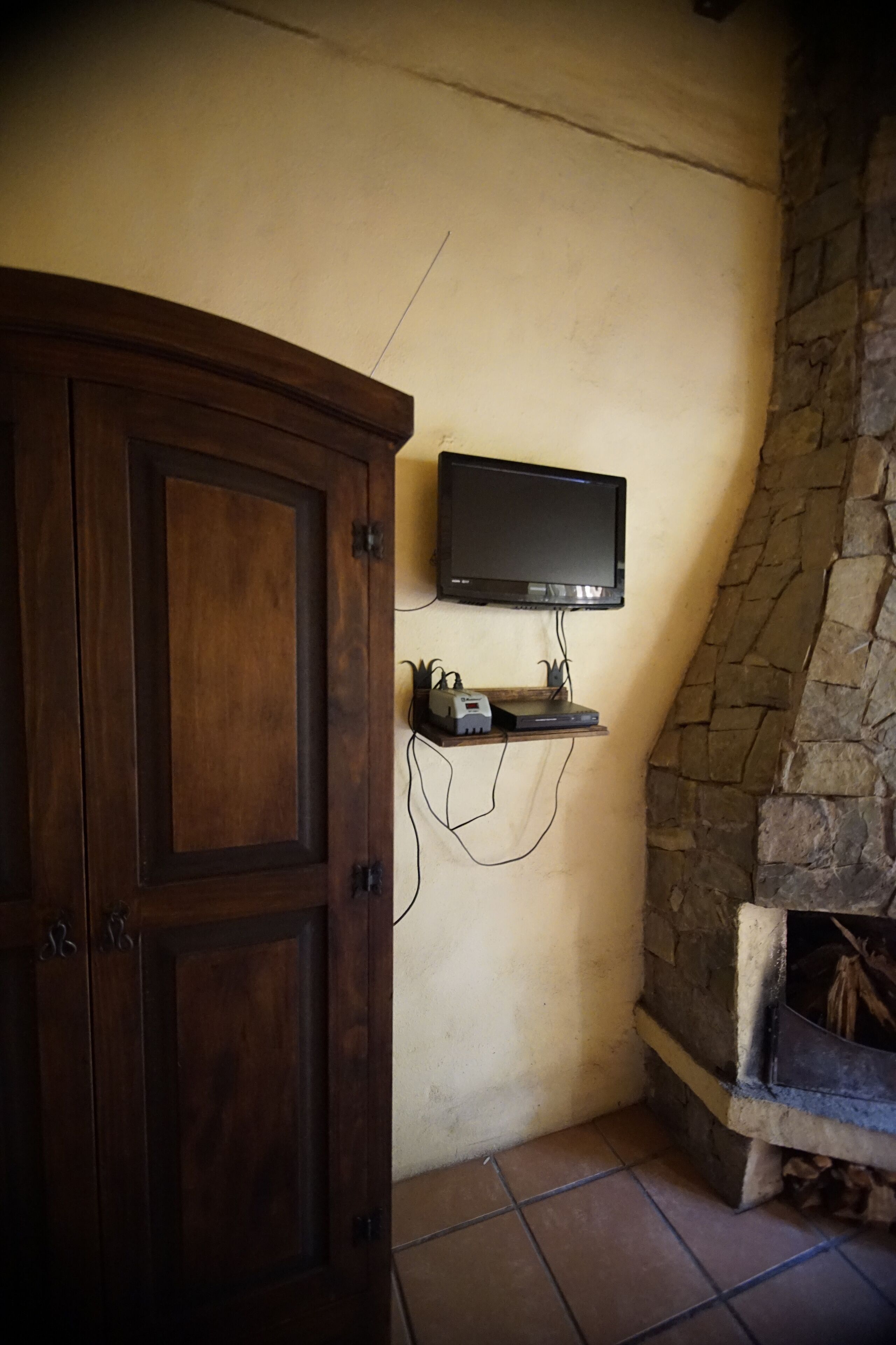 A room with a wooden cabinet, a mounted television, and a stone wall.