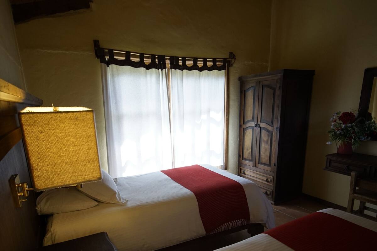 Una habitación con dos camas, un armario de madera, un escritorio y una lámpara.