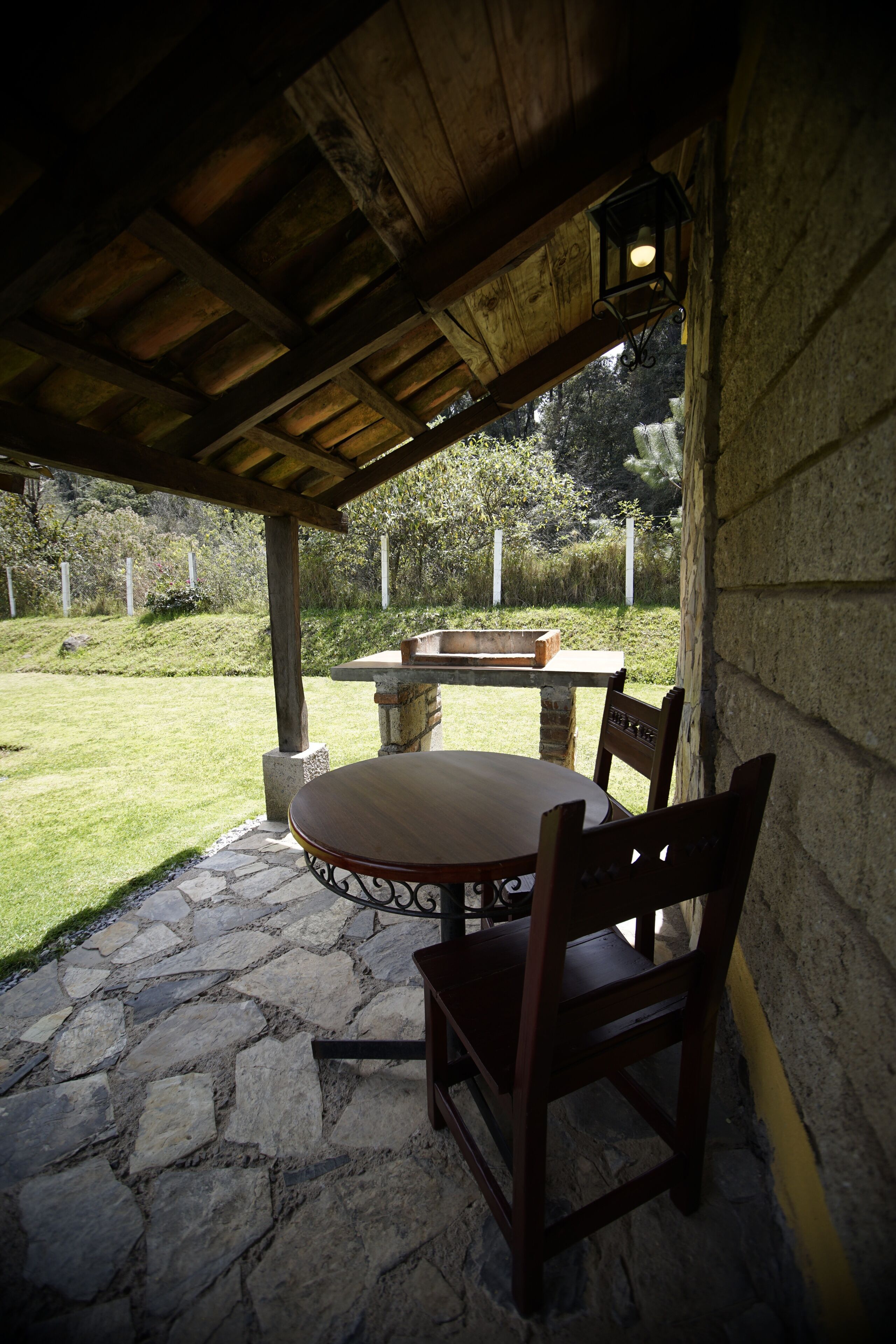 Un patio al aire libre con una mesa y sillas de piedra, un pozo de fuego y vistas a un área verde.