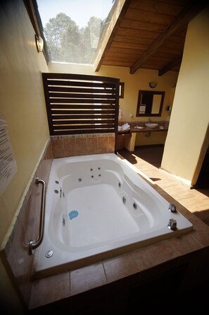 A bathroom with a large bathtub, a wooden ceiling, and a view of the outdoors. - Cabañas La Cascada (Zacatlán)