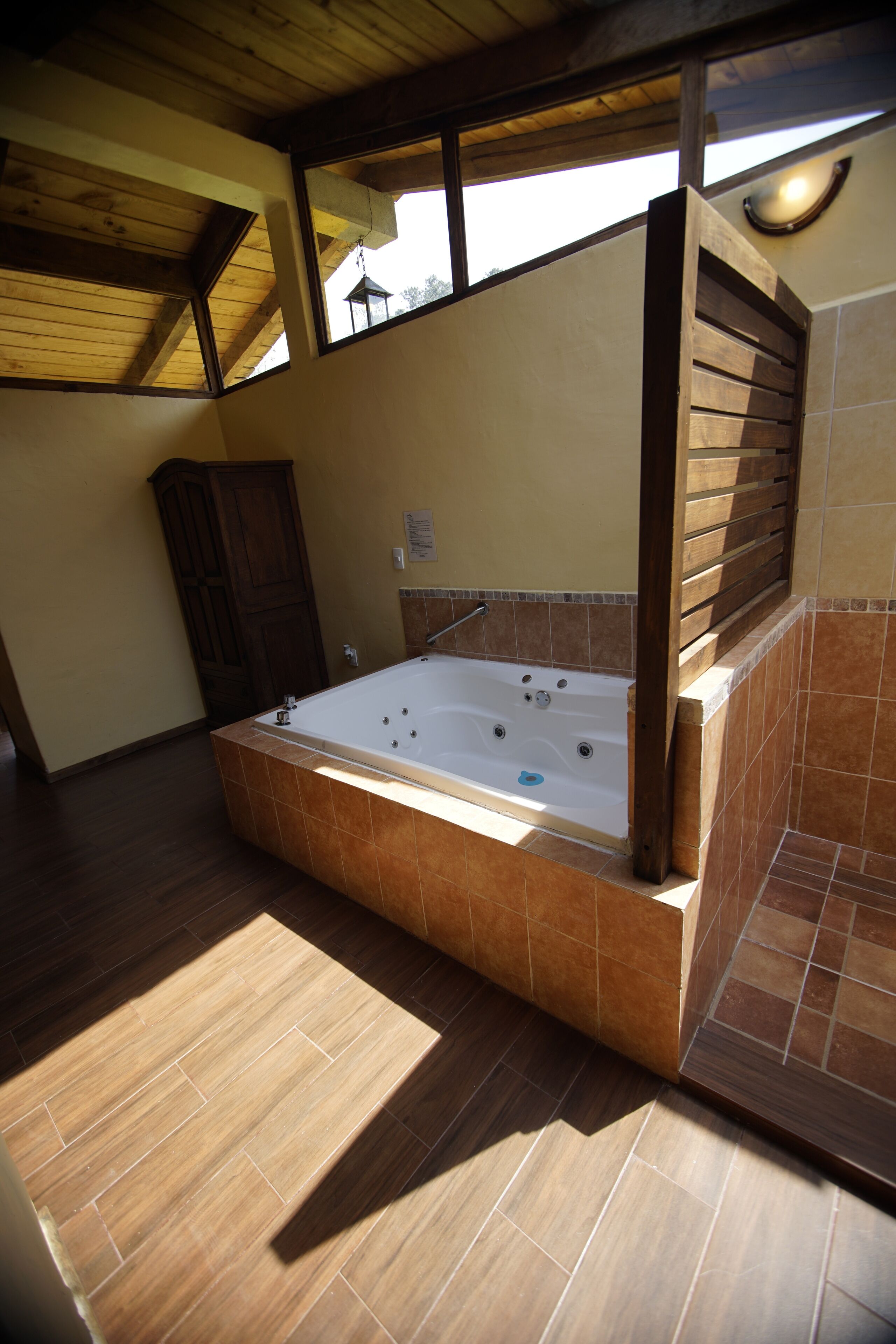 Un baño espacioso con una bañera grande, vigas de madera en el techo y vistas a través de una ventana.