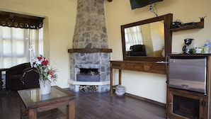 Una sala de estar con chimenea de piedra, vigas de madera en el techo, un televisor de pantalla plana y una mesa de centro con flores.