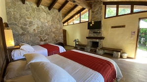 Una habitación con dos camas, paredes de piedra, una chimenea y un ventanal grande.