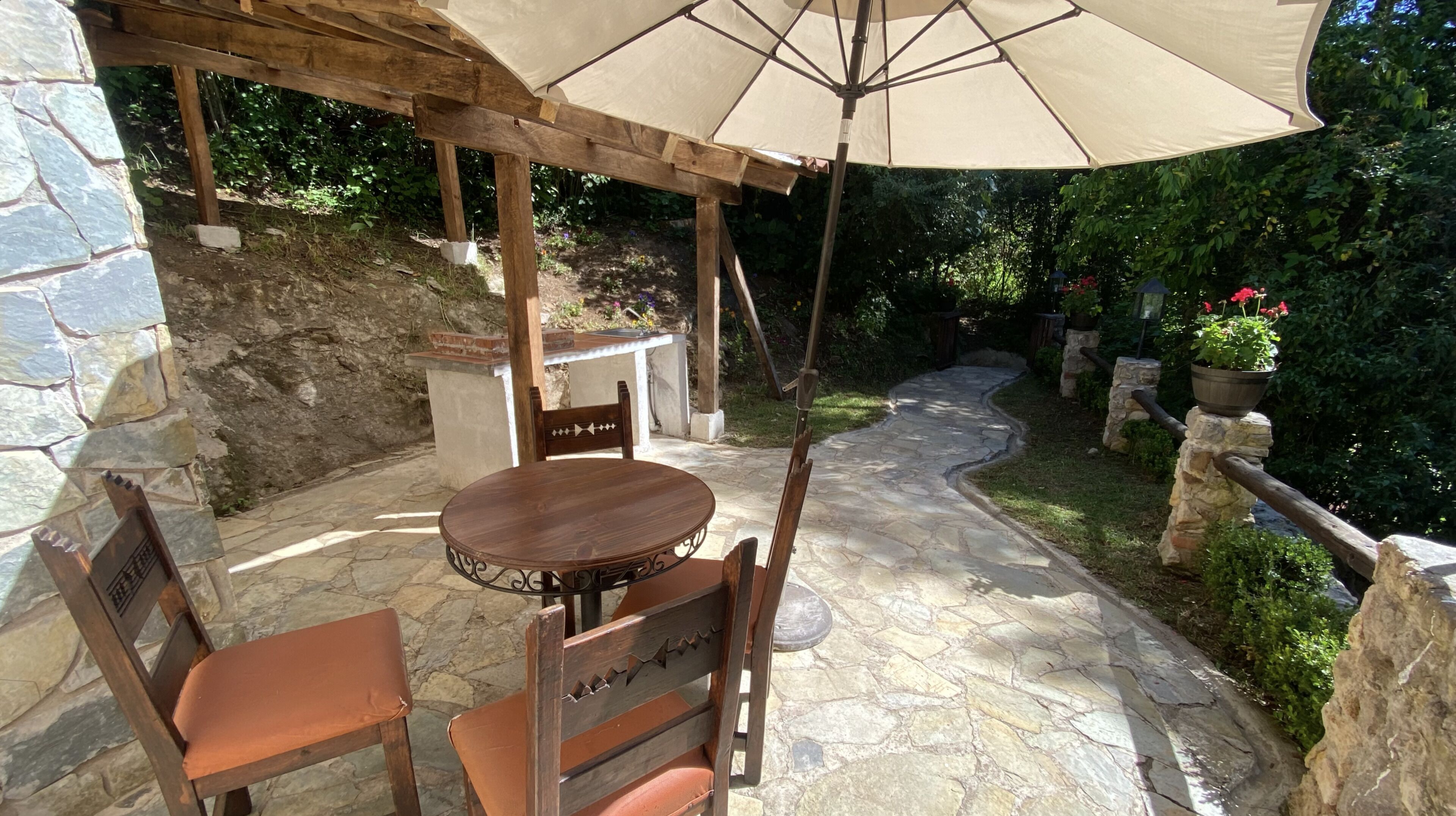An outdoor patio with a stone table and chairs, a wooden pergola, and a stone pathway.
