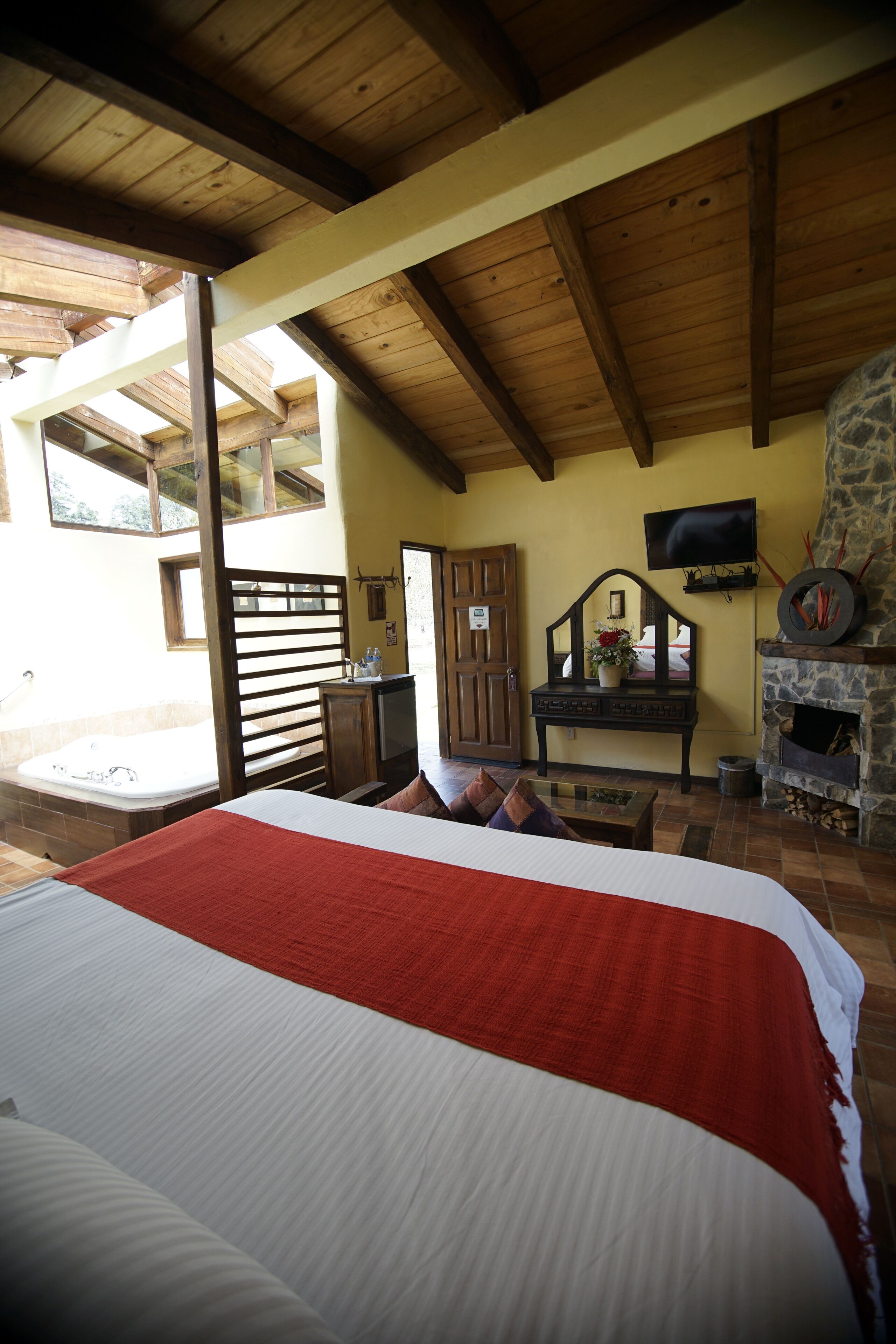 Un dormitorio con una cama grande, vigas de madera, una chimenea de piedra y un televisor en la pared.