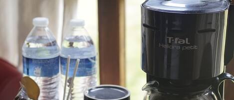 A coffee maker on a table with two water bottles and a glass container.