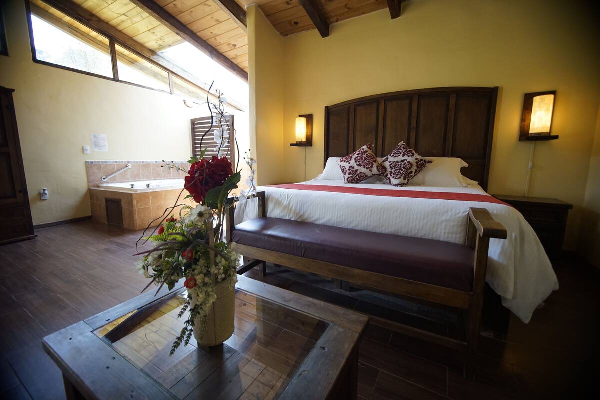 Un dormitorio con cama de madera, un banco, un jarrón de flores y una bañera.
