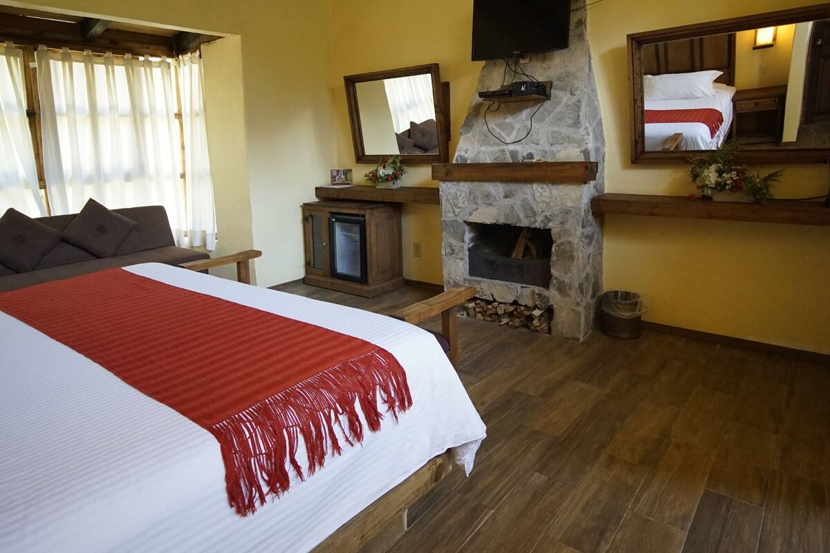Un dormitorio con una cama grande, vigas de madera, una chimenea de piedra, un televisor y un espejo sobre la cama.