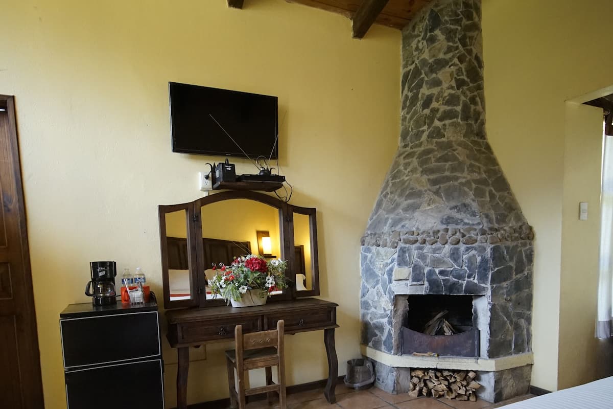 Un dormitorio con chimenea de piedra, un escritorio con espejo y una cama con manta roja.