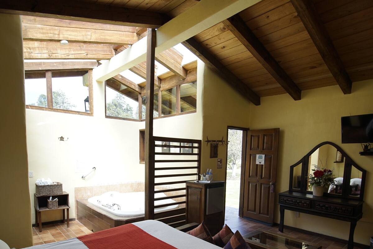 Un dormitorio con una cama grande, techo de madera, una mesita y vistas al exterior.