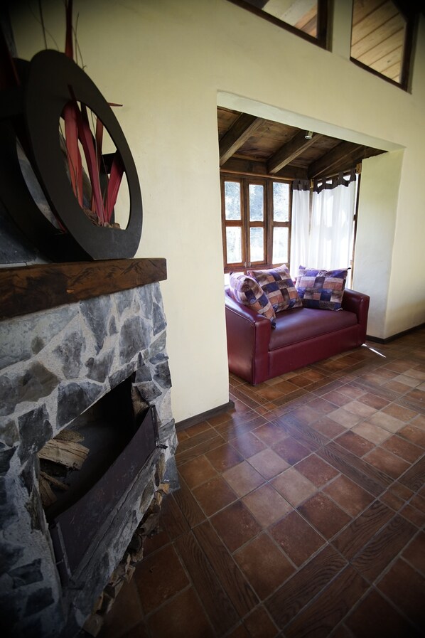 Una sala de estar con chimenea de piedra, un sofá rojo con cojines estampados y techo de madera.