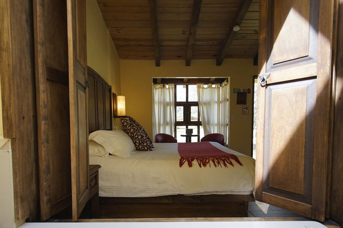 Un dormitorio con una cama grande, paredes de madera, una ventana con cortinas y una bañera blanca.