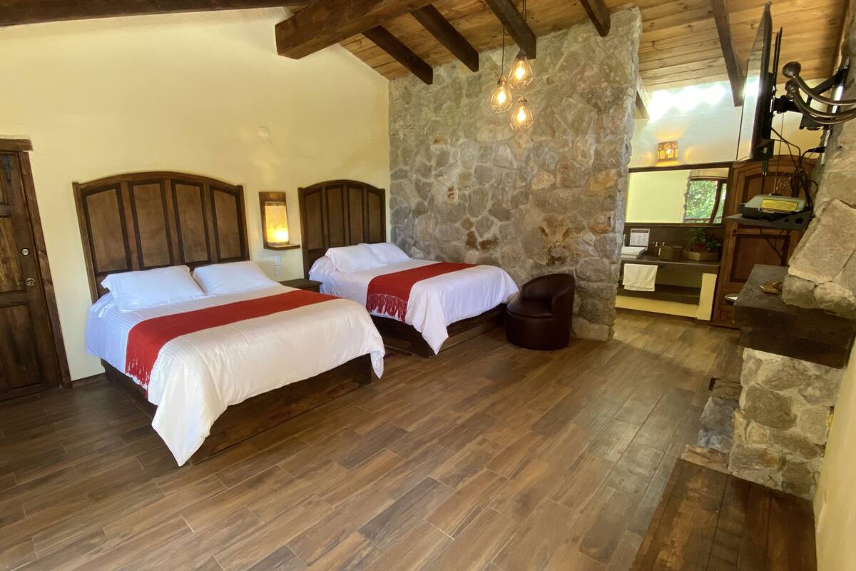 Habitación con dos camas, suelo de madera, paredes de piedra y chimenea de piedra.