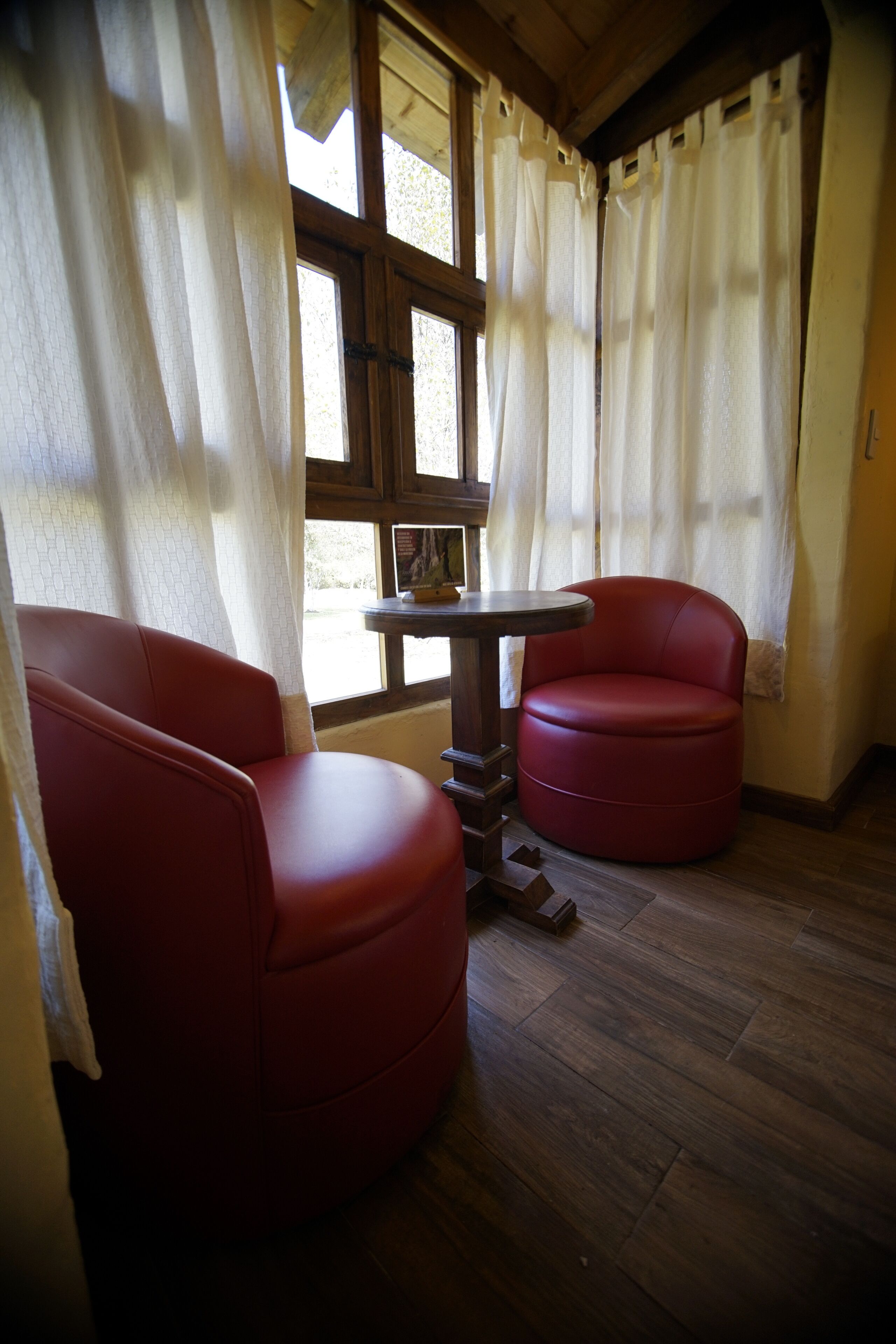 Une pièce avec deux fauteuils en cuir rouge, une petite table ronde et une fenêtre avec des rideaux.