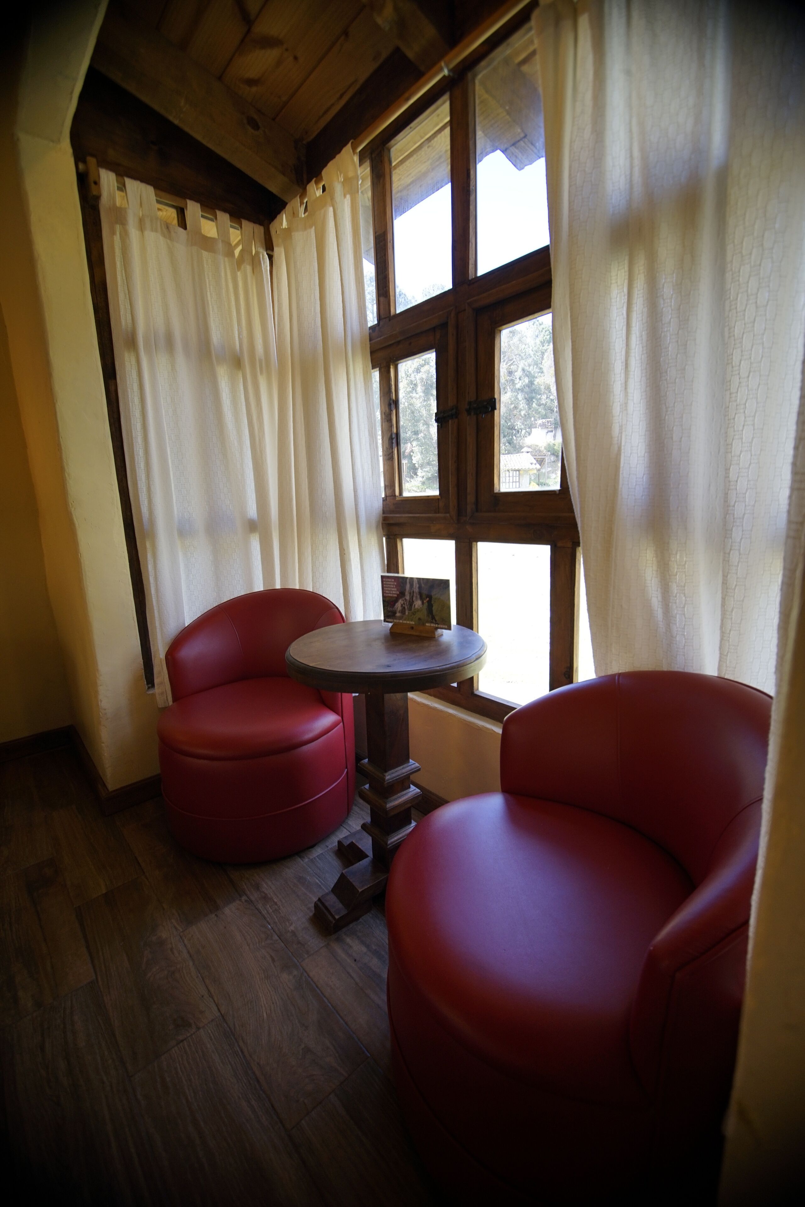 A room with two red chairs, a small round table, and a window with curtains.