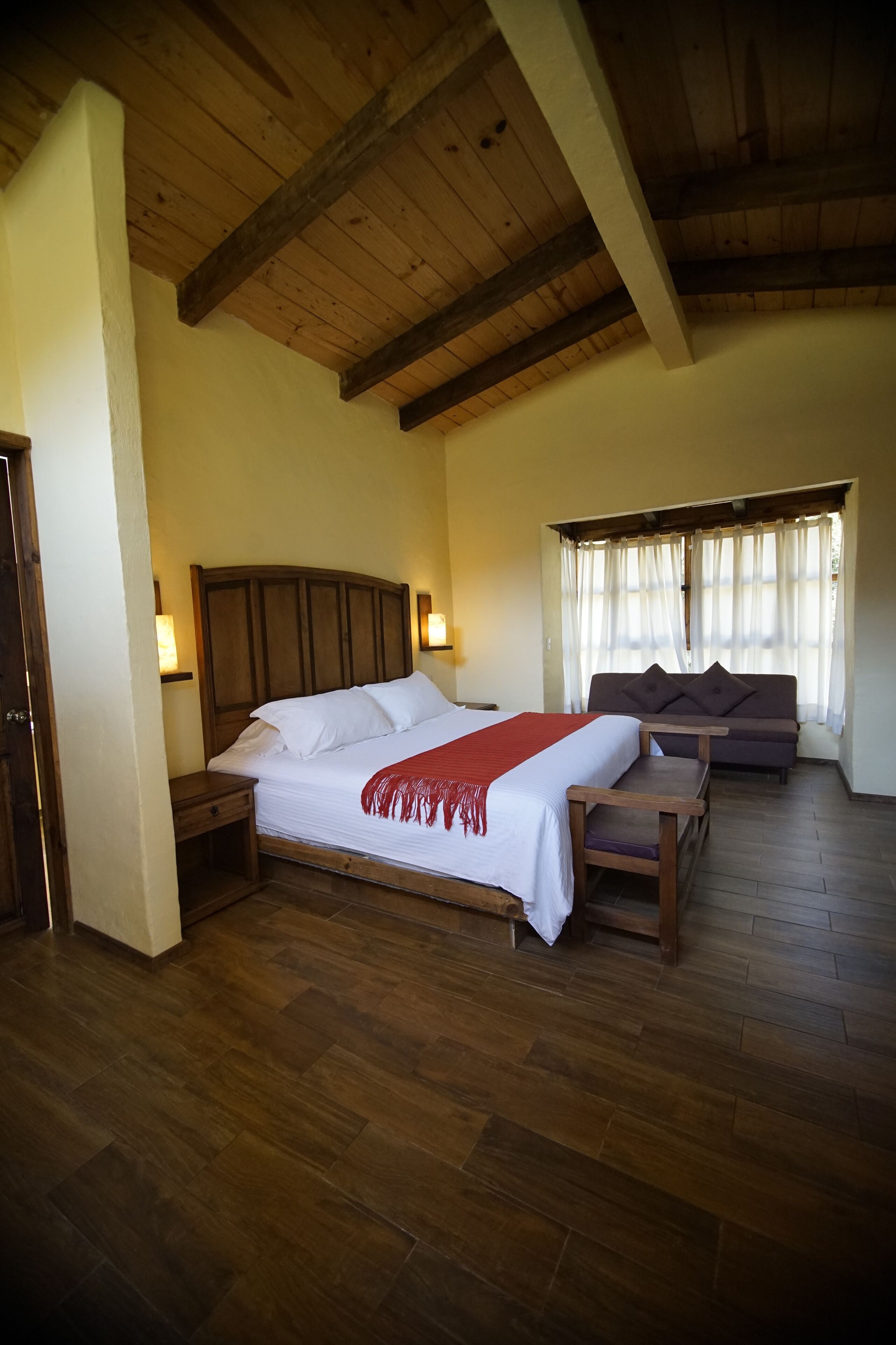 Een slaapkamer met een houten bed, nachtkastjes, een bank en een raam met gordijnen.