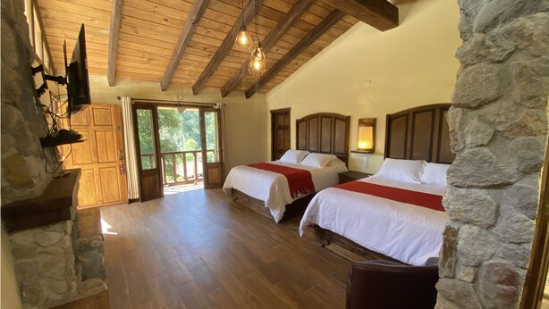 Una habitación con dos camas, piso de madera, paredes de piedra y un ventanal grande.