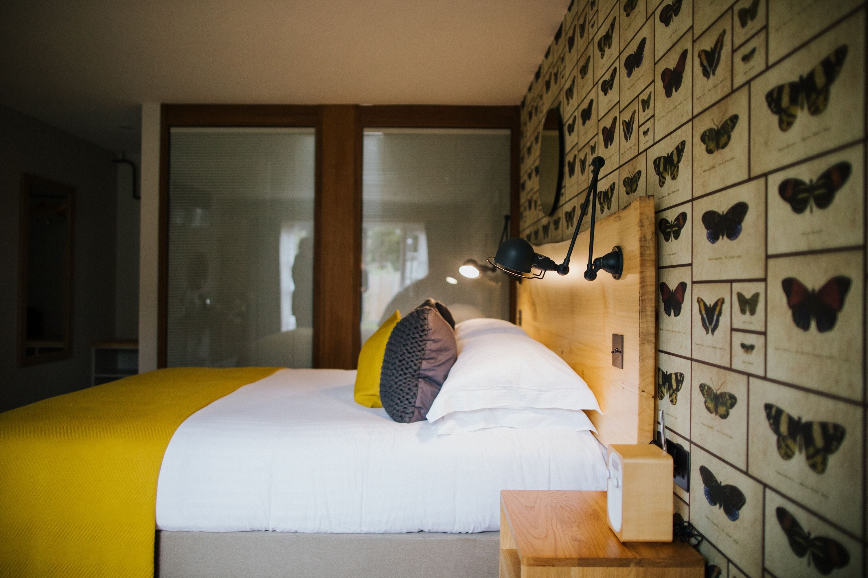 Een slaapkamer met een bed, een nachtkastje, een wandlamp en een wanddecoratie met vlinders.