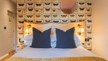 Una habitación de hotel con una cama, dos lámparas de noche, una pared llena de estampas de mariposas y un cabecero de madera.