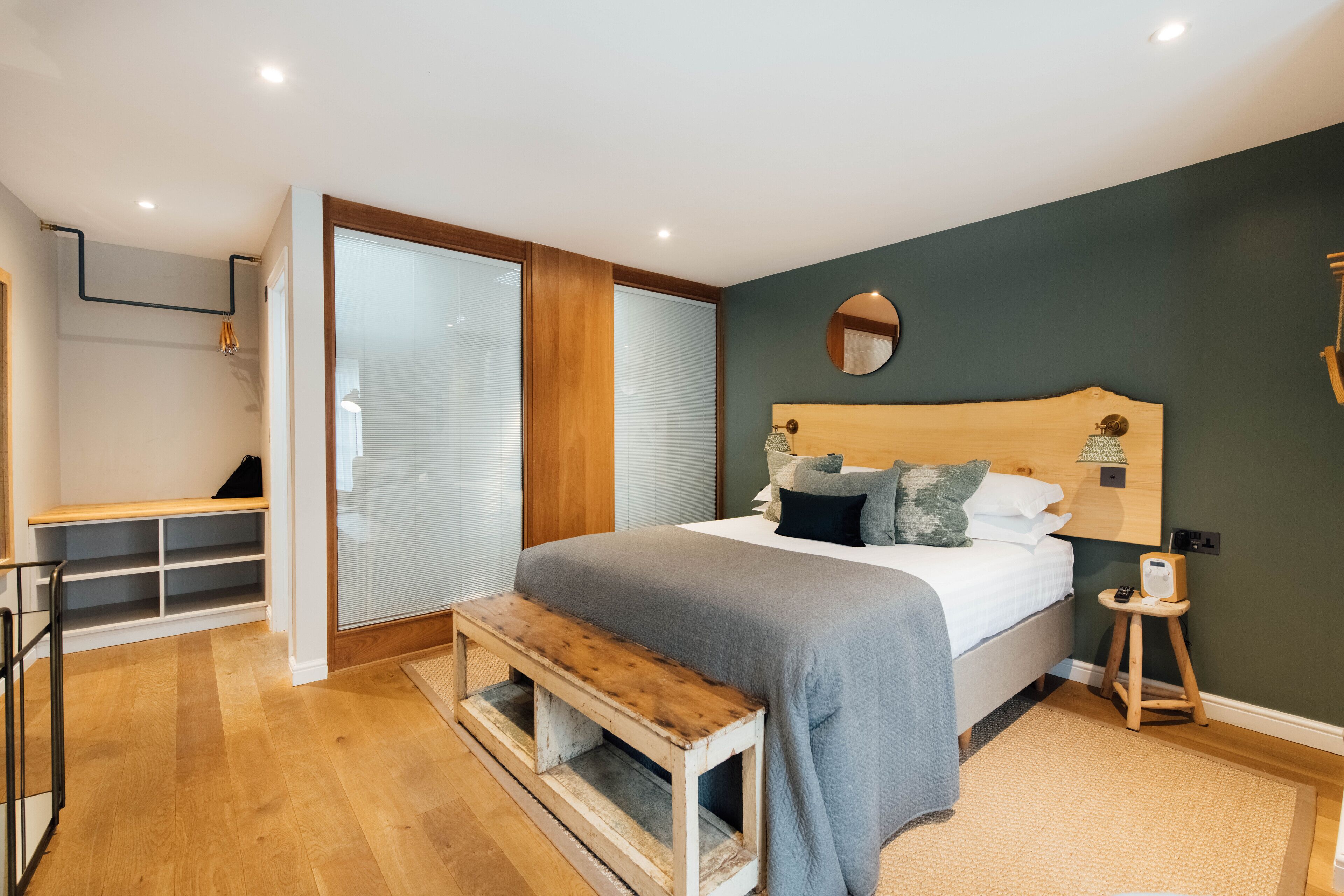 Un dormitorio con una cama, un banco, un taburete pequeño y un espejo en la pared.