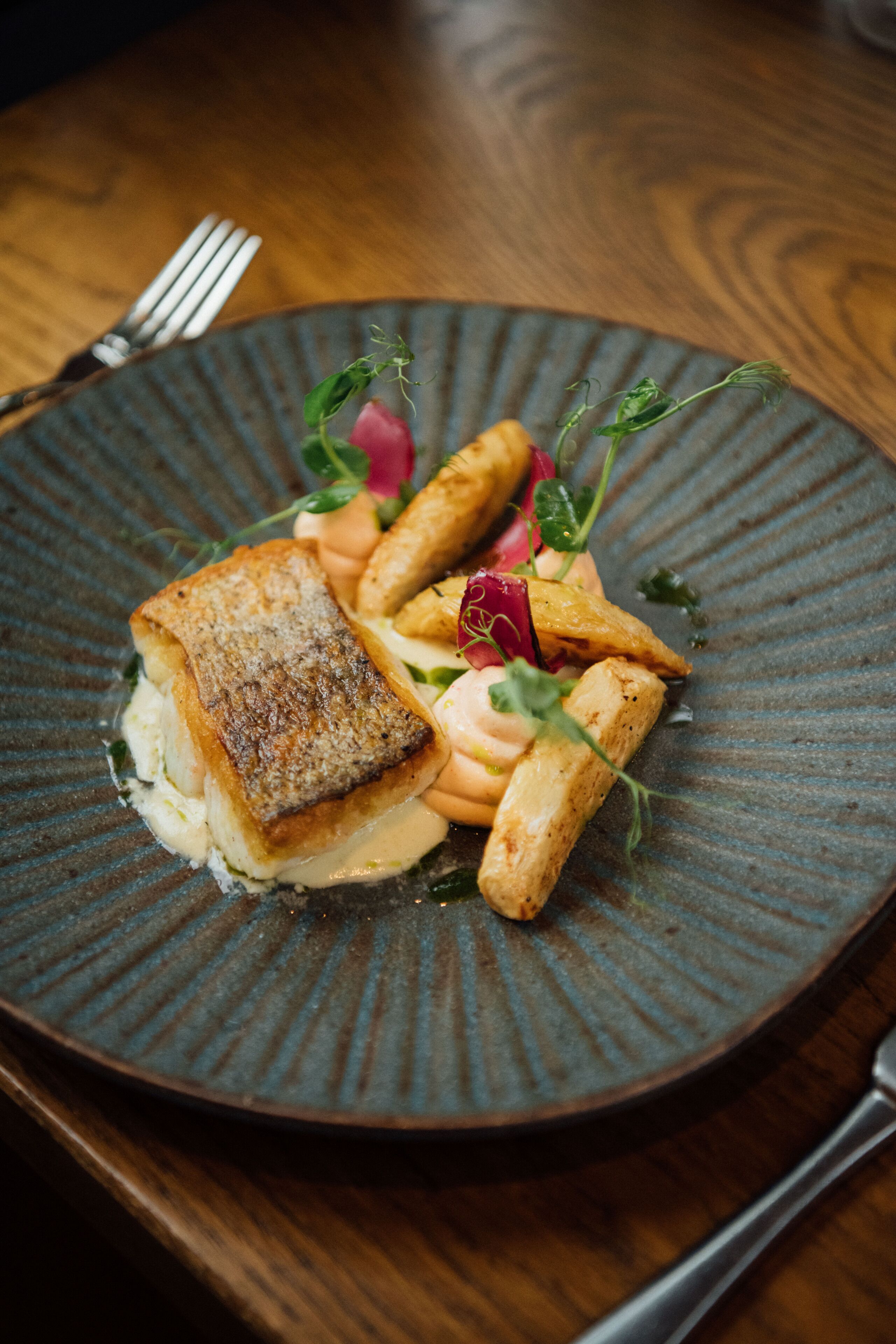 Un plato de comida con un trozo de pescado y verduras sobre un plato con textura.