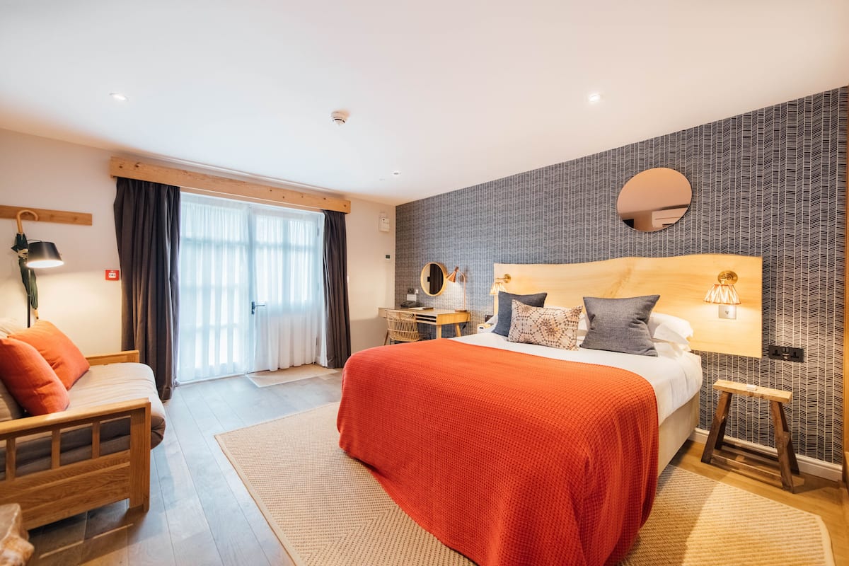 A modern bedroom with a large bed, a desk, and a mirror.