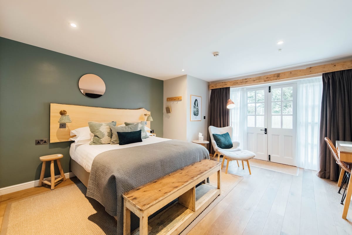 A bedroom with a bed, bedside table, chair, bench, and a view of the outside through a large window.