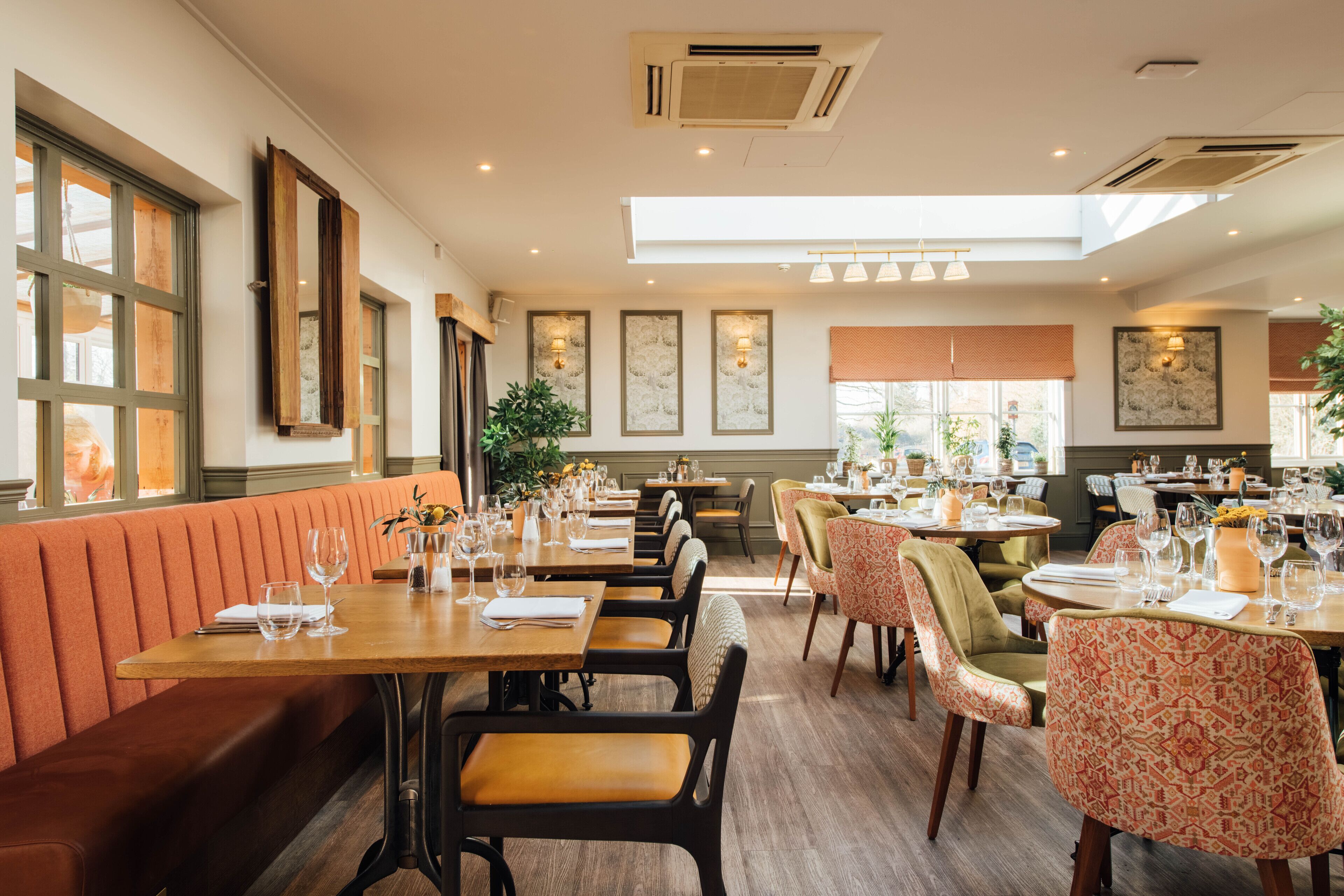 Un restaurante con mesas y sillas de madera, techo alto y ventanas amplias.