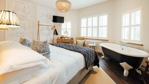 A bedroom with a large bed, a black bathtub, and a desk with a chair. - The Fox at Willian  (Letchworth)